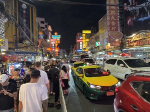 Crowds and yellow-and-green taxis on Yaowarat Road beneath illuminated signs in Bangkok’s Chinatown at night.
